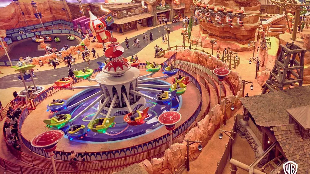 Amusement park ride with colorful cars around a central structure, surrounded by other attractions and visitors.