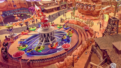 Amusement park ride with colorful cars around a central structure, surrounded by other attractions and visitors.