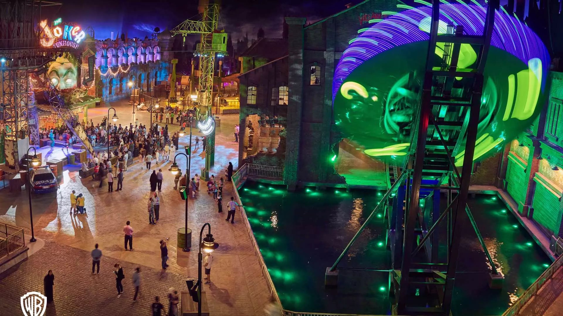 Colorful nighttime scene at a theme park with vibrant lights and people walking around.