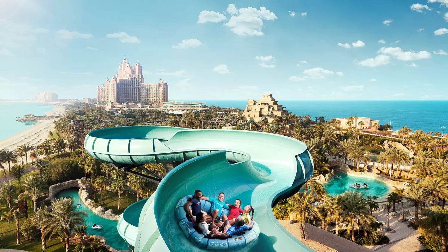 People on a water slide at a tropical resort with ocean and skyline in the background
