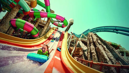 Colorful water slide at an amusement park with a child in a green shirt.